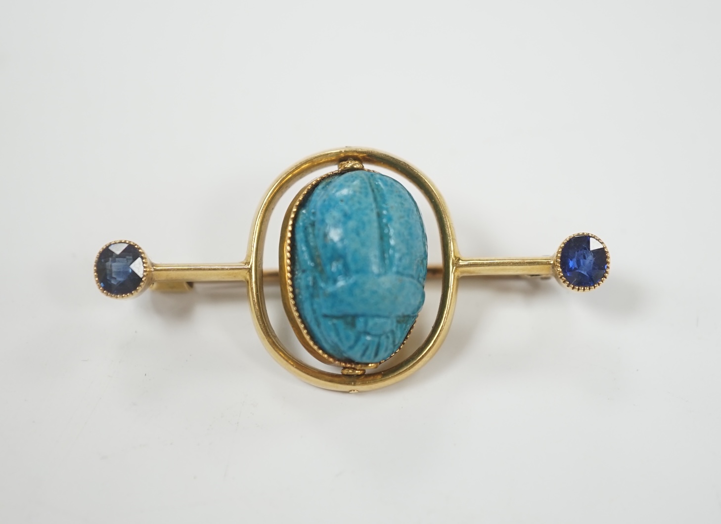 A yellow metal and two stone sapphire set swivelling scarab bar brooch, 41mm, gross weight 5.7 grams.